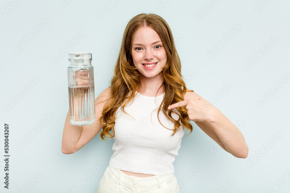 Young caucasian woman holding jar of water isolated on blue background person pointing by hand to a shirt copy space, proud and confident Young caucasian woman holding jar of water isolated on blue background person pointing by hand to a shirt copy space, proud and confident