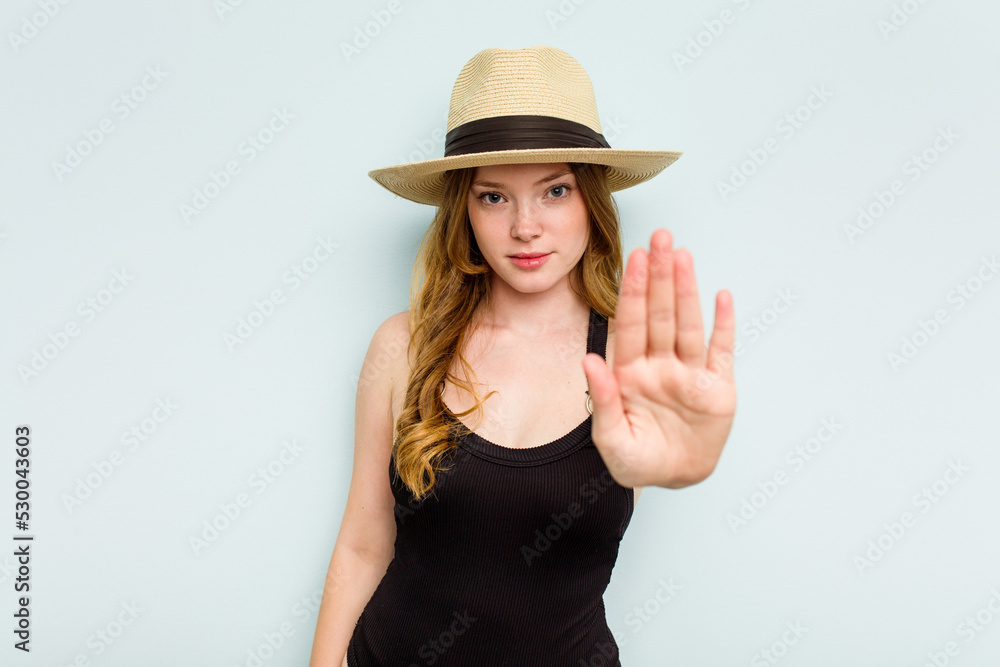 Young caucasian woman going to the beach isolated on blue background standing with outstretched hand showing stop sign, preventing you. Young caucasian woman going to the beach isolated on blue background standing with outstretched hand showing stop sign, preventing you.
