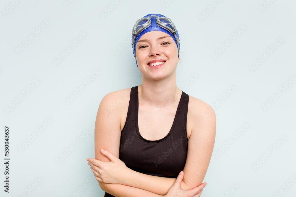 Young caucasian swimmer woman isolated on blue background laughing and having fun. Young caucasian swimmer woman isolated on blue background laughing and having fun.