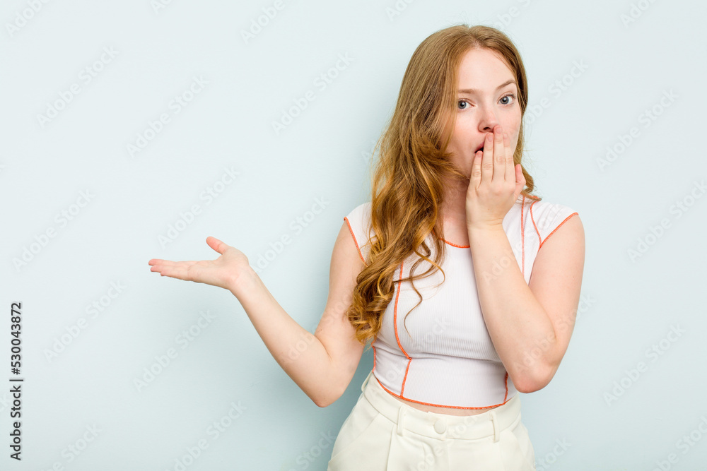 Young caucasian woman isolated on blue background impressed holding copy space on palm. Young caucasian woman isolated on blue background impressed holding copy space on palm.