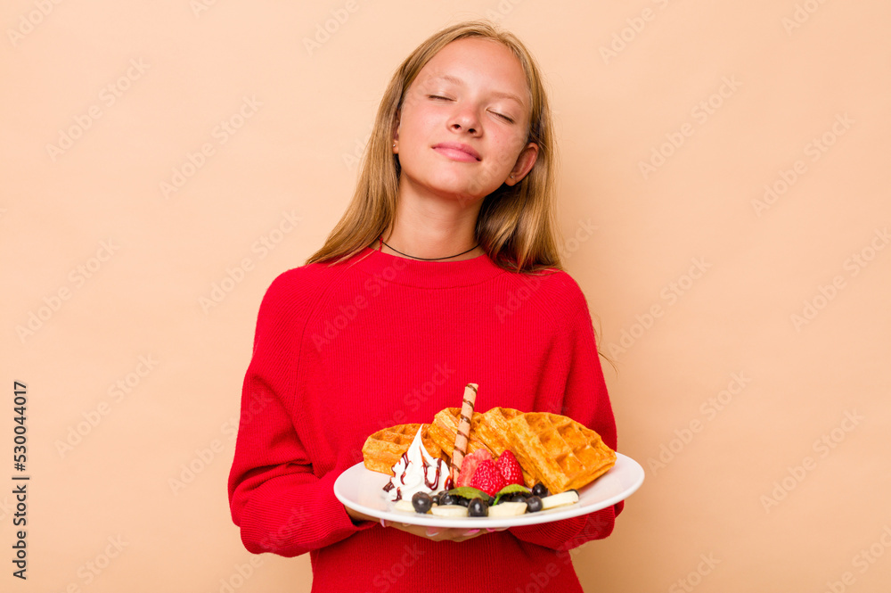 Little caucasian girl holding a waffles isolated on beige background dreaming of achieving goals and purposes Little caucasian girl holding a waffles isolated on beige background dreaming of achieving goals and purposes