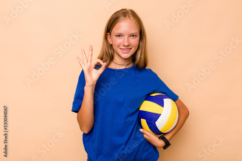 Little caucasian girl playing volleyball isolated on beige background cheerful and confident showing ok gesture.