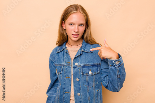 Caucasian teen girl isolated on beige background person pointing by hand to a shirt copy space, proud and confident