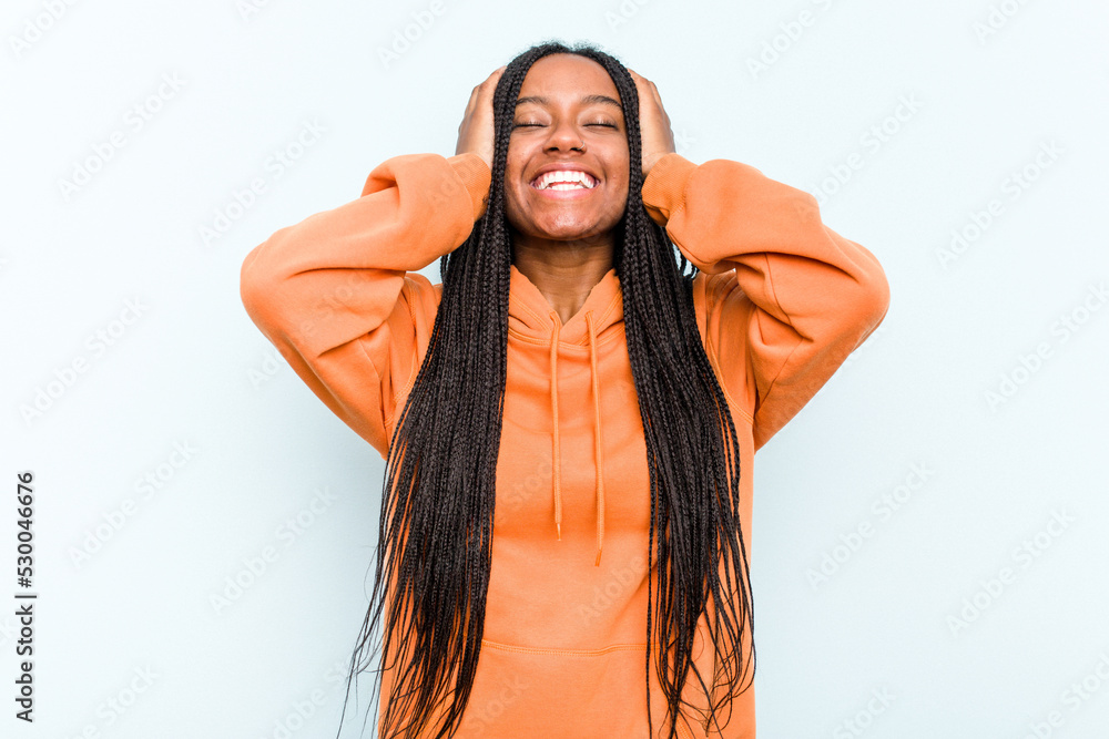 Young African American woman with braids hair isolated on blue background laughs joyfully keeping hands on head. Happiness concept.