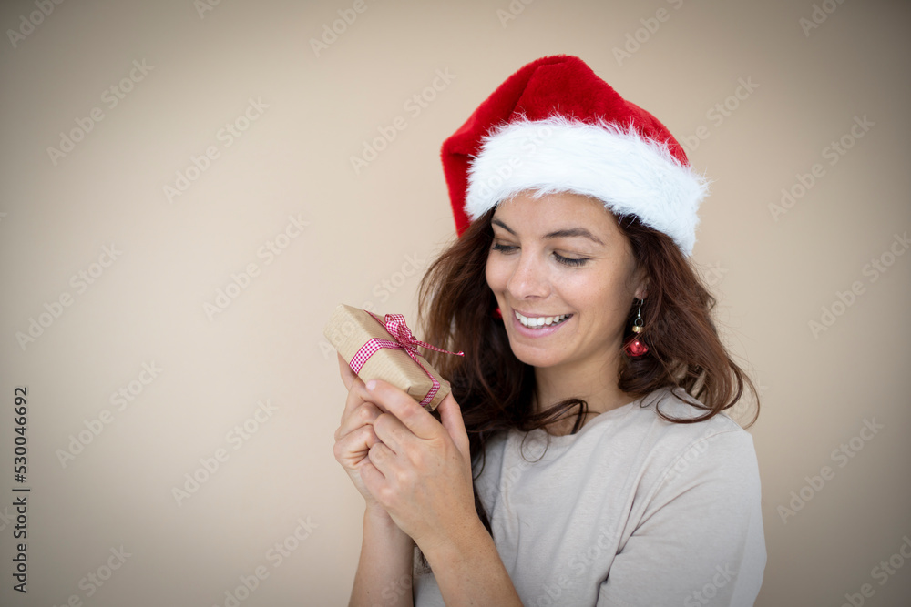 pretty young woman with beautiful long hair holds a small christmas gift in her hand and has earrings that look like christmas tree balls and a santa hat on pretty young woman with beautiful long hair holds a small christmas gift in her hand and has earrings that look like christmas tree balls and a santa hat on