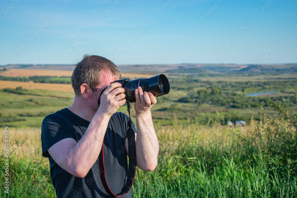 Photographer takes aim and takes pictures of nature outdoors while in the field in summer Photographer takes aim and takes pictures of nature outdoors while in the field in summer