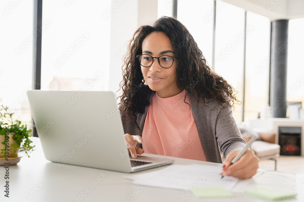 Young african student tutor freelancer businesswoman doing homework, paperwork for college, preparing for test exam, using laptop online at home office Young african student tutor freelancer businesswoman doing homework, paperwork for college, preparing for test exam, using laptop online at home office