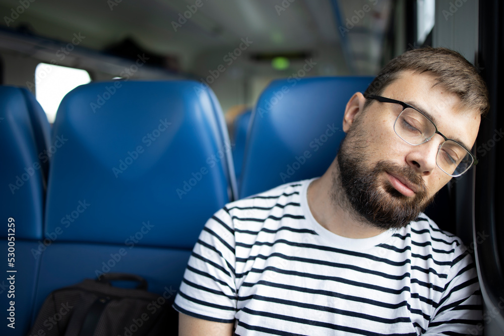 Close-up of a man in glasses and a striped T-shirt sleeping in a carriage. Concept: travel, communication, mobile phone, adventure. Lonely traveler resting in a train while traveling