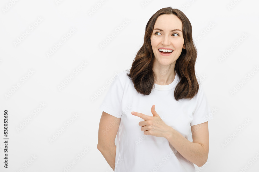 online advertising of goods and services, smiling brunette woman in white T-shirt looks and points finger to side on white background online advertising of goods and services, smiling brunette woman in white T-shirt looks and points finger to side on white background