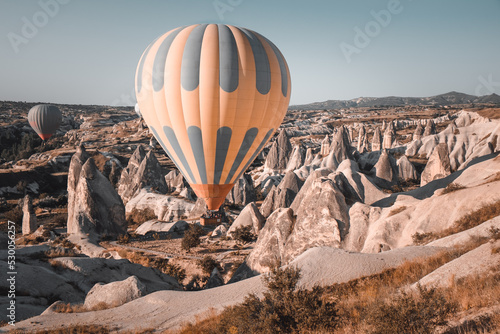 Colorful hot air balloon preparing to rise up for sunset watching tour over spectacular Cappadocia mountains. Wide landscape of Goreme valley. Vintage retro orange blue toning filter. Tourism, travel