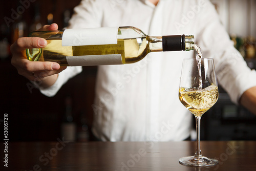 Obraz na płótnie Male sommelier pouring white wine into long-stemmed wineglasses.