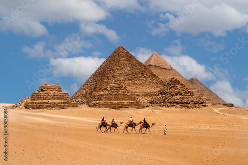 Cairo, Egypt. 08.25.2022. Group of tourists riding camels seeing the pyramids of Menkaure, Chephren and Cheops.