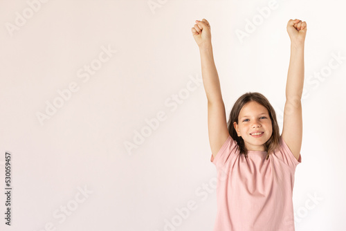 Portrait of happy preteen girl wearing pink T-shirt raising arms. Caucasian child looking at camera and smiling. Happiness concept