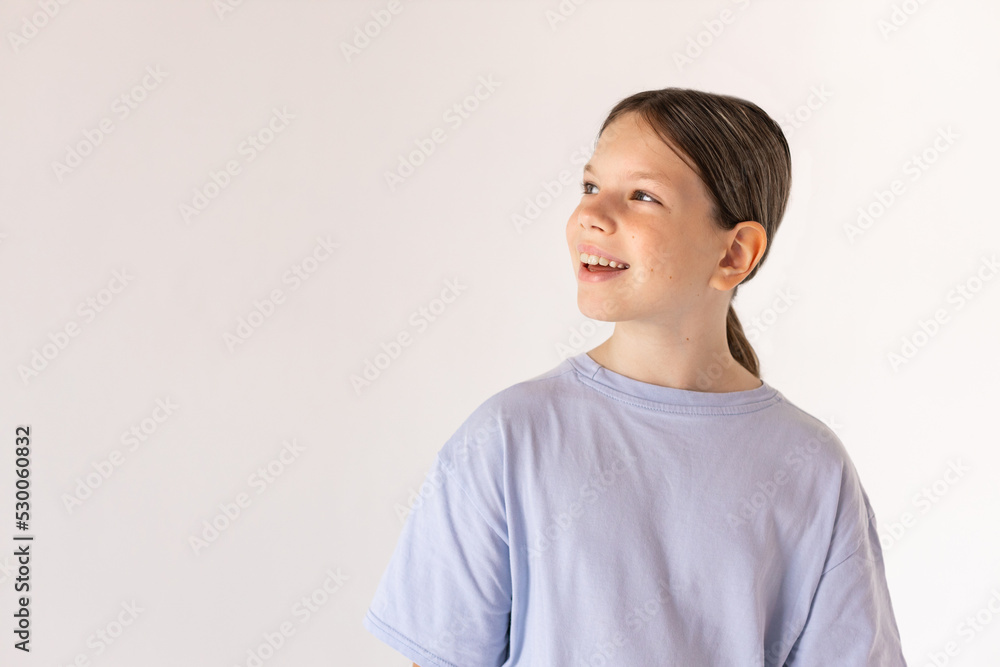 Portrait of happy preteen girl wearing blue T-shirt looking away. Caucasian child smiling against white background. Happiness and curiosity concept Portrait of happy preteen girl wearing blue T-shirt looking away. Caucasian child smiling against white background. Happiness and curiosity concept