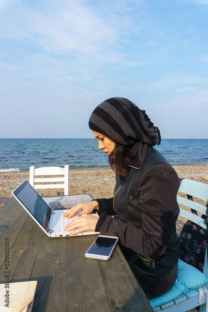 Woman working on laptop on beach. Digital nomadism, remote and freelance working everywhere on sunny day concept idea. Empty copy space son sky for advertising texts.