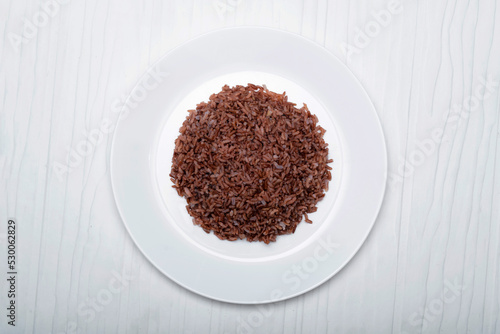 Asian food cooked red rice in plate isolated on white wood background.