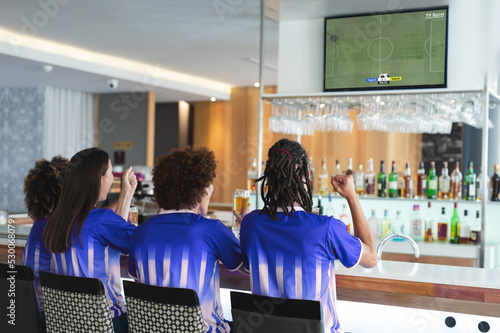 Diverse friends in bar watching tv with football match on screen