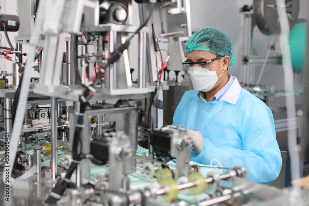 Worker in personal protective equipment or PPE inspecting quality of mask and medical face mask production line in factory, manufacturing industry and factory concept. Worker in personal protective equipment or PPE inspecting quality of mask and medical face mask production line in factory, manufacturing industry and factory concept.