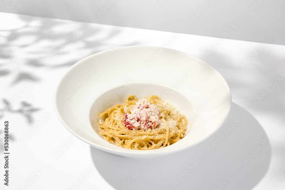 Spaghetti with crab meat and cheese on white table with shadows. Seafood pasta with spaghetti and crab in summer italian menu Italian pasta with parmigiano cheese and crab meat