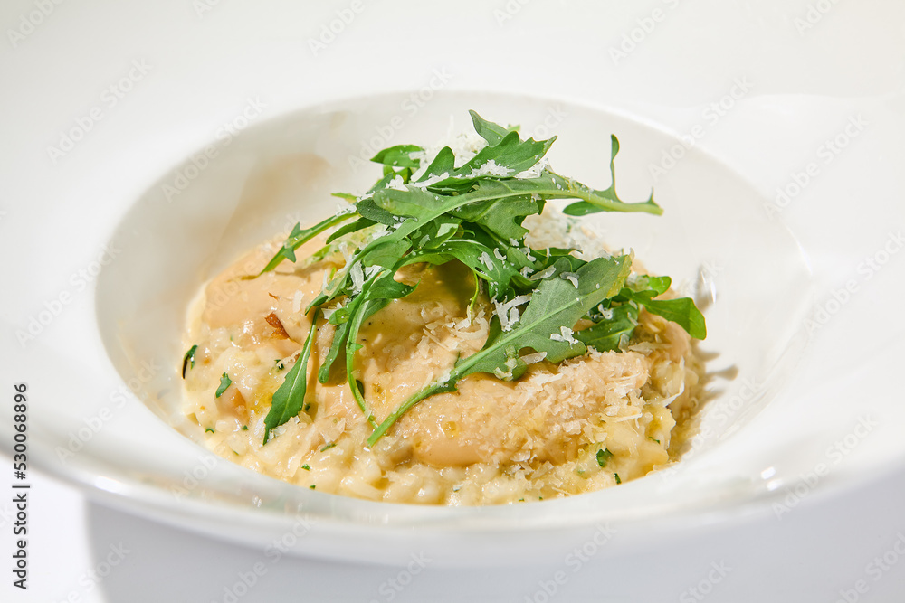 Italian cheese risotto on white plate. Creamy risotto topped parmesan cheese and espuma. Italian risotto with cheese on light background with shadows of leaves Simple italian menu