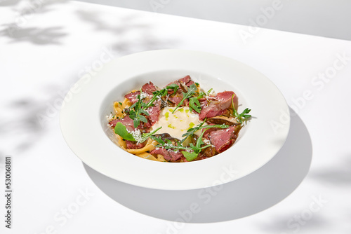 Homemade pasta with pastrami and creamy sauce with cheese. Italian pasta pappardelle with beef and sauce on white table Italian food in summer dining with shadows of sunlight