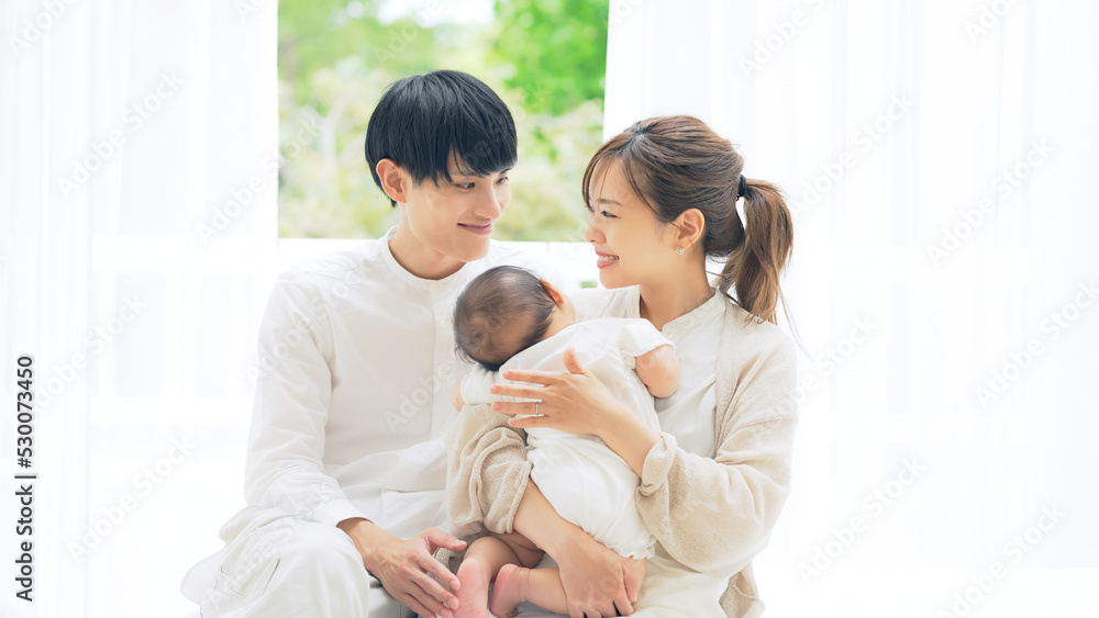 部屋でくつろぐ赤ちゃんを抱いたカップル　家族イメージ