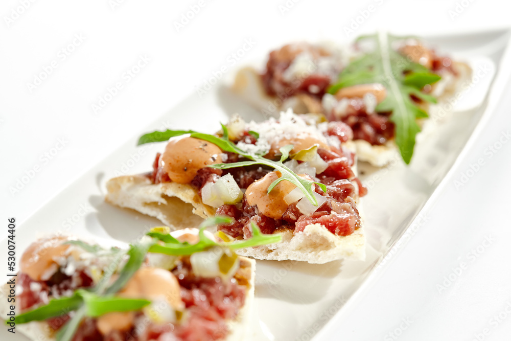 Beef tartare on crispy focaccia isolated on white background. Appetizer from minced meat with spicy sauce on toast.  Starter food meat tartare in French style. Contemporary food for restaurant.