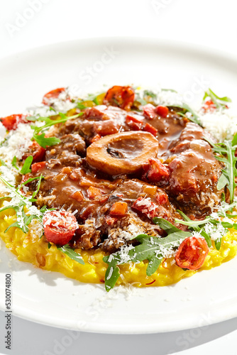 Traditional Italian dish - osso buco with risotto Milanese and cherry tomato and rucola. Ossobuco with saffron rice isolated on white background. Stewed meat on bone with yellow risotto.