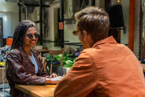 happy african american woman in sunglasses looking at blurred friend in outdoor cafe terrace. © LIGHTFIELD STUDIOS