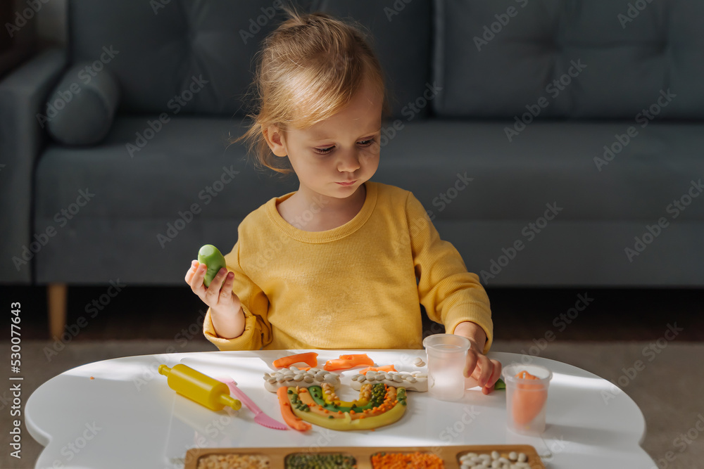 A little girl playing with rainbow from play dough for modeling with decorate from dried beans