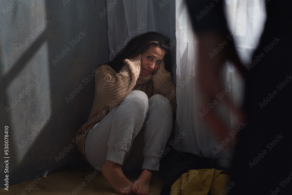 Scared woman sitting on ground and crying in fear of domestic violence. Scared woman sitting on ground and crying in fear of domestic violence.