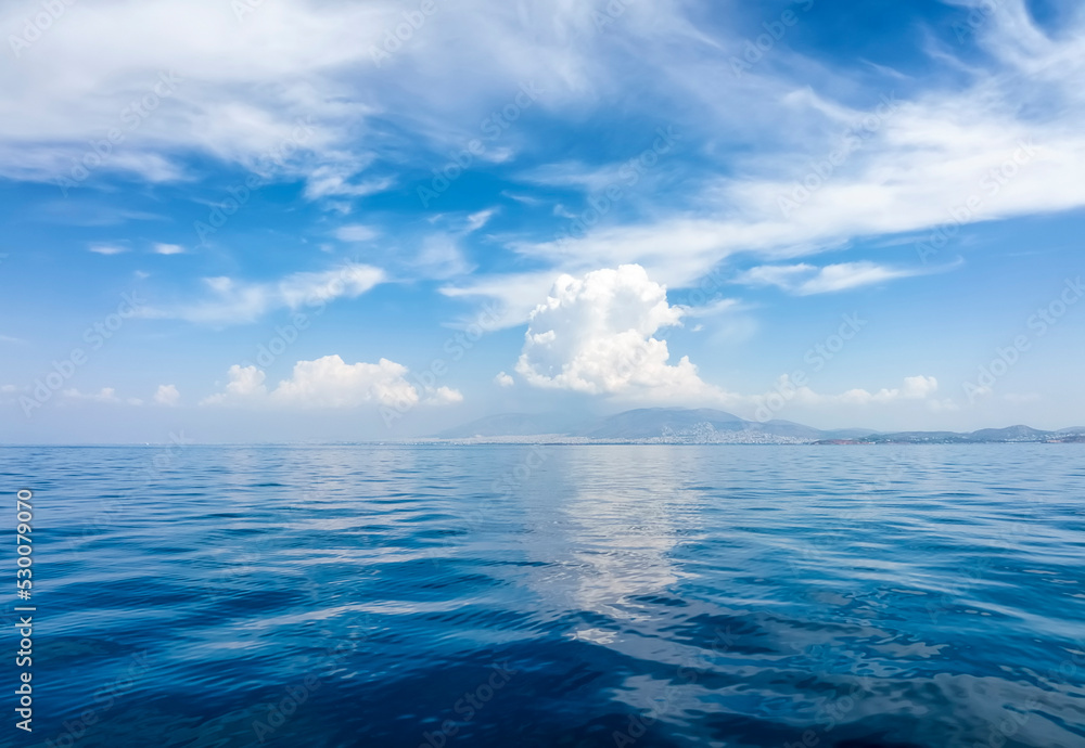 A background of a calm ocean with blue sky and white clouds and reflections in the water