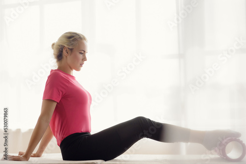 Healthy athletic woman using foam roller while having workout at home