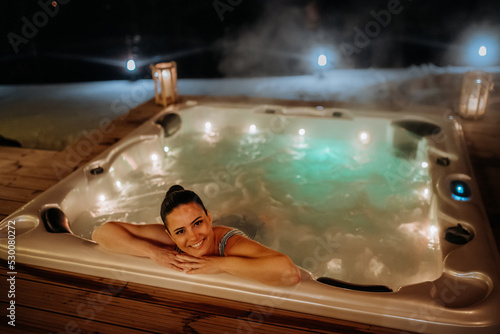 Young woman enjoying outdoor bathtub in her terrace during cold winter evening. photo