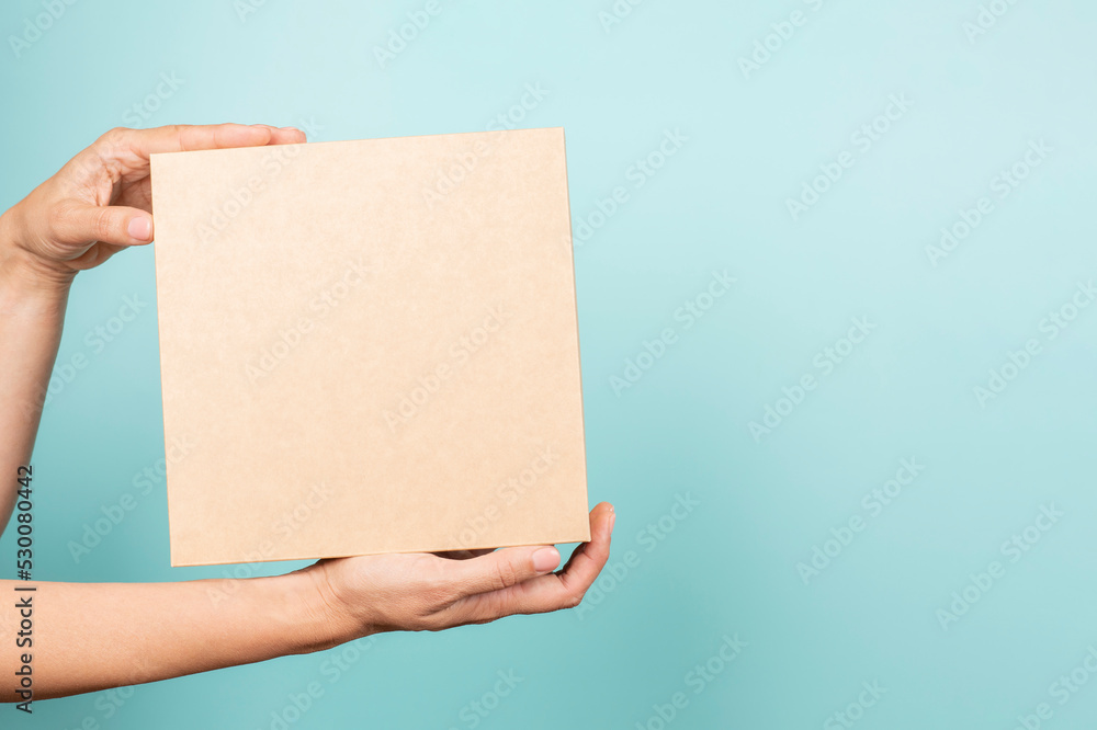 Woman hand show brown rectangular cardboard box on light blue background. Mockup parcel box. Packaging, shopping, delivery, present, gift concept Woman hand show brown rectangular cardboard box on light blue background. Mockup parcel box. Packaging, shopping, delivery, present, gift concept