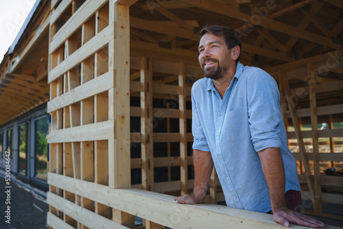 Man looking out of his unfinished house, construction of ecological renewable low energy sustainable wooden eco house .