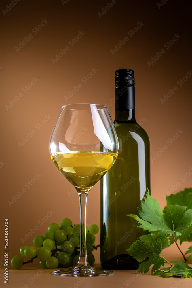 Bottle, glass of white wine and grapes with vine