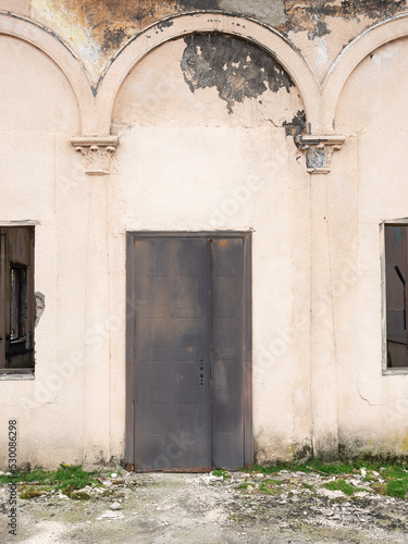 Rusty door of an abandoned building with arched decor on the wall.