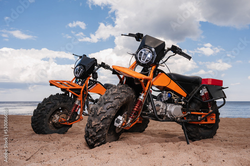 Two custom off-road sports motorcycles are parked on the beach outdoors