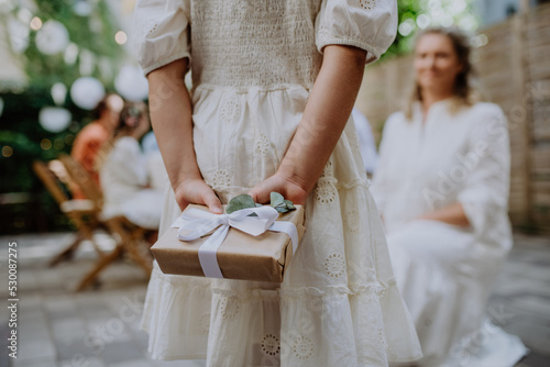 Rear view of little child giving wedding gift to mature bride at wedding backyard party. photo