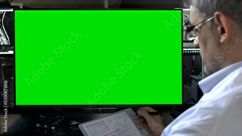 doctor holding a clipboard and looking at green screen monitor
