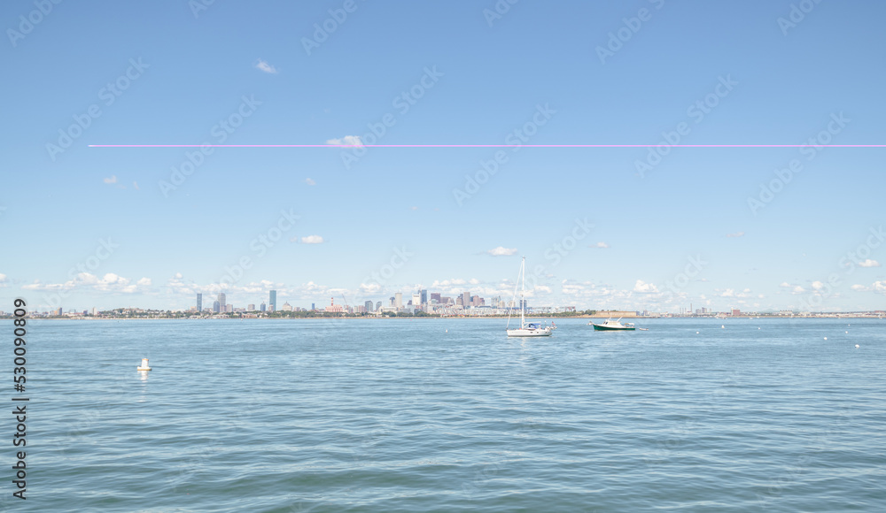 Boats in the harbor with the Boston skyline wide view in the far distance.