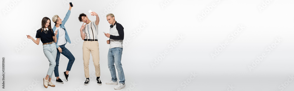 Obraz premium happy friends taking selfie on mobile phones and dancing on grey background, banner.