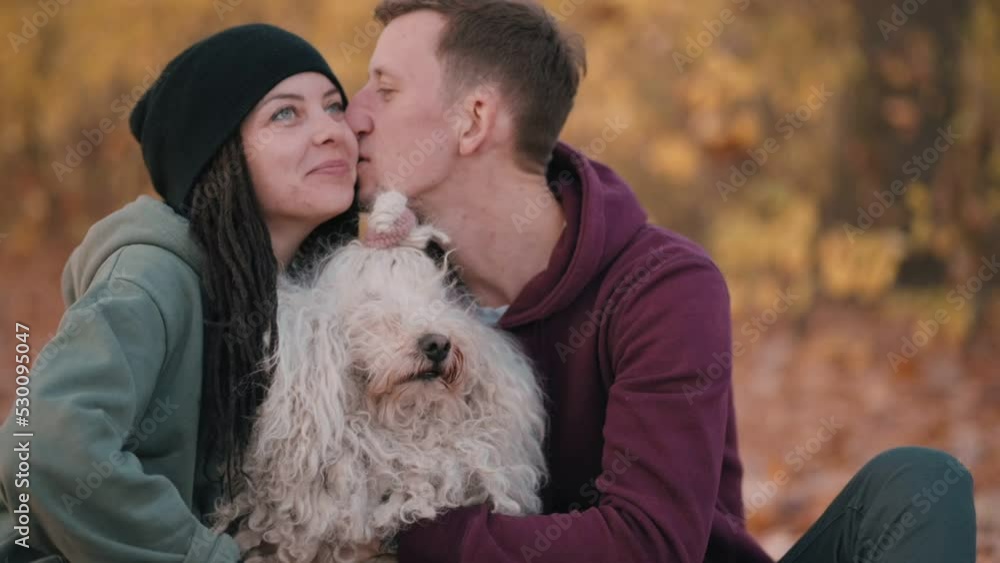 Couple playing with dog. Young happy couple petting their pet while sitting on fallen leaves. Hungarian Shepherd Dog Buli breed in nature. Couple playing with dog. Young happy couple petting their pet while sitting on fallen leaves. Hungarian Shepherd Dog Buli breed in nature.
