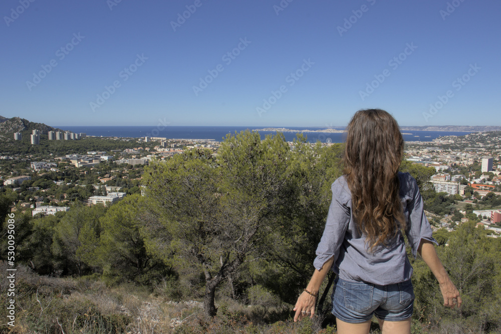 A woman stands in front of a landscape of city, nature and sea. A woman stands in front of a landscape of city, nature and sea.