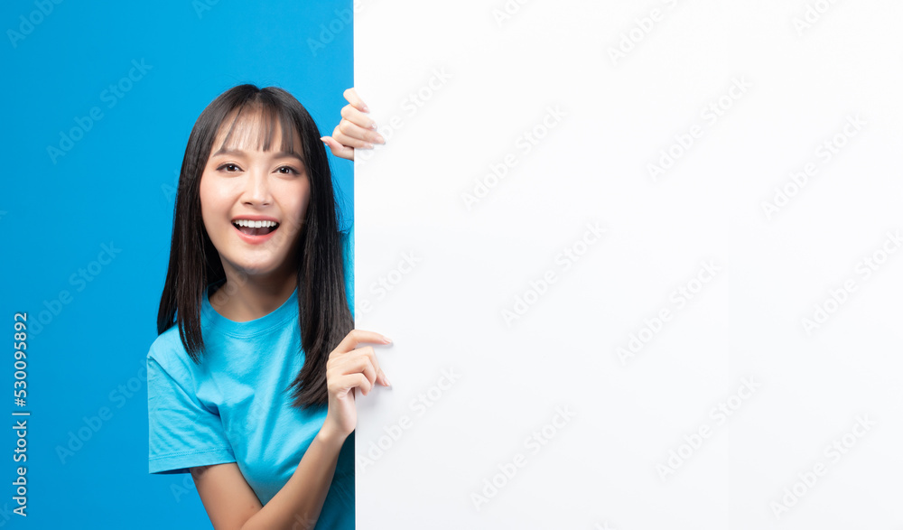 Portrait of smiling asian woman holding empty blank board on blue studio background. Happy young girl standing with white square paper card for text and showing card to camera. Portrait of smiling asian woman holding empty blank board on blue studio background. Happy young girl standing with white square paper card for text and showing card to camera.