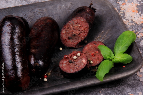fried whole and sliced blood sausage on a black clay plate, gray stone background,Traditional Latvian blood sausages © SHARKY PHOTOGRAPHY