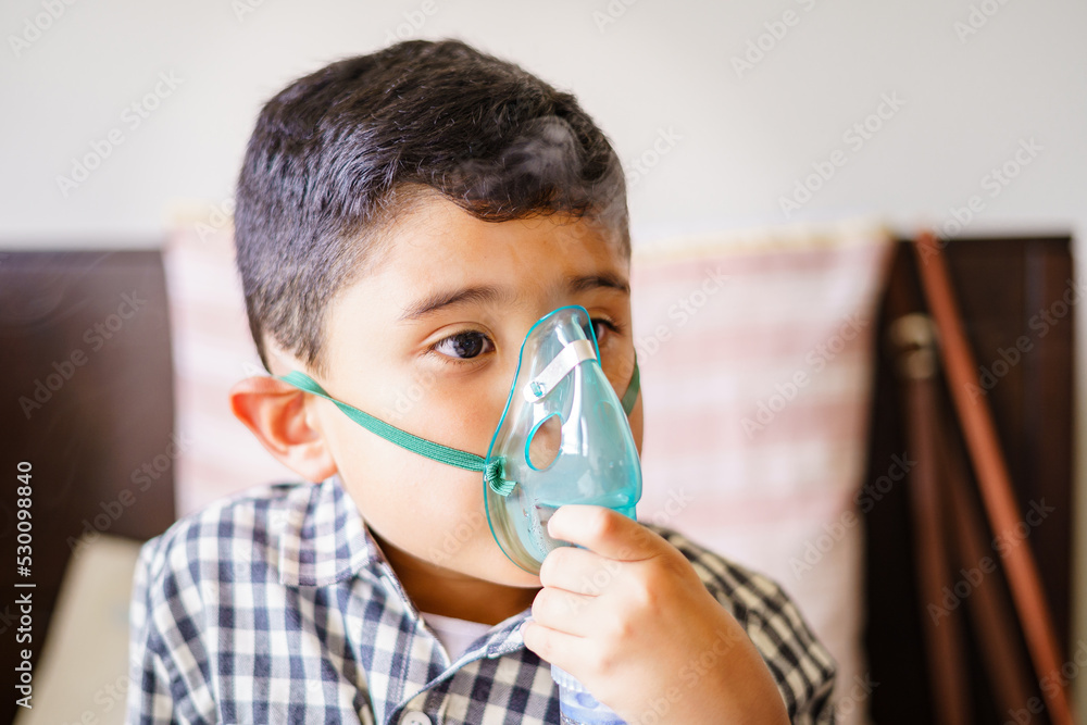 Sick child inhaling with nebulizer to reduce cough, lying at home