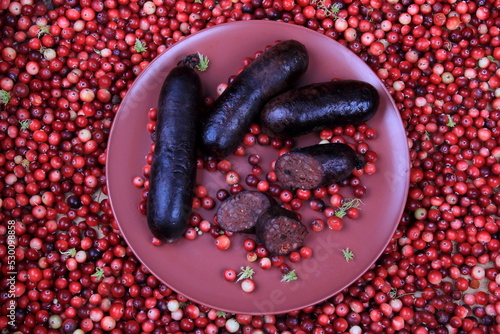 Baked blood sausage on a red plate decorated with red cranberries, Traditional Latvian blood sausages