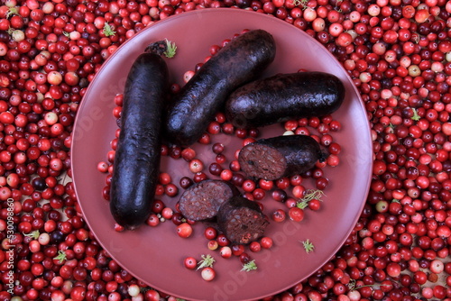 Baked blood sausage on a red plate decorated with red cranberries, Traditional Latvian blood sausages photo